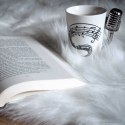 Biały kubek do herbaty, ze wzorem pięciolini i srebrnym uchem w kształcie srebrnego mikrofonu.